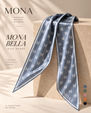 A MONA Bella silk scarf in a dusty blue-gray color with a repeating cream monogram pattern, draped elegantly over a beige stone pedestal. The image features elegant typography on the left and a vertical row of color swatches on the bottom right.